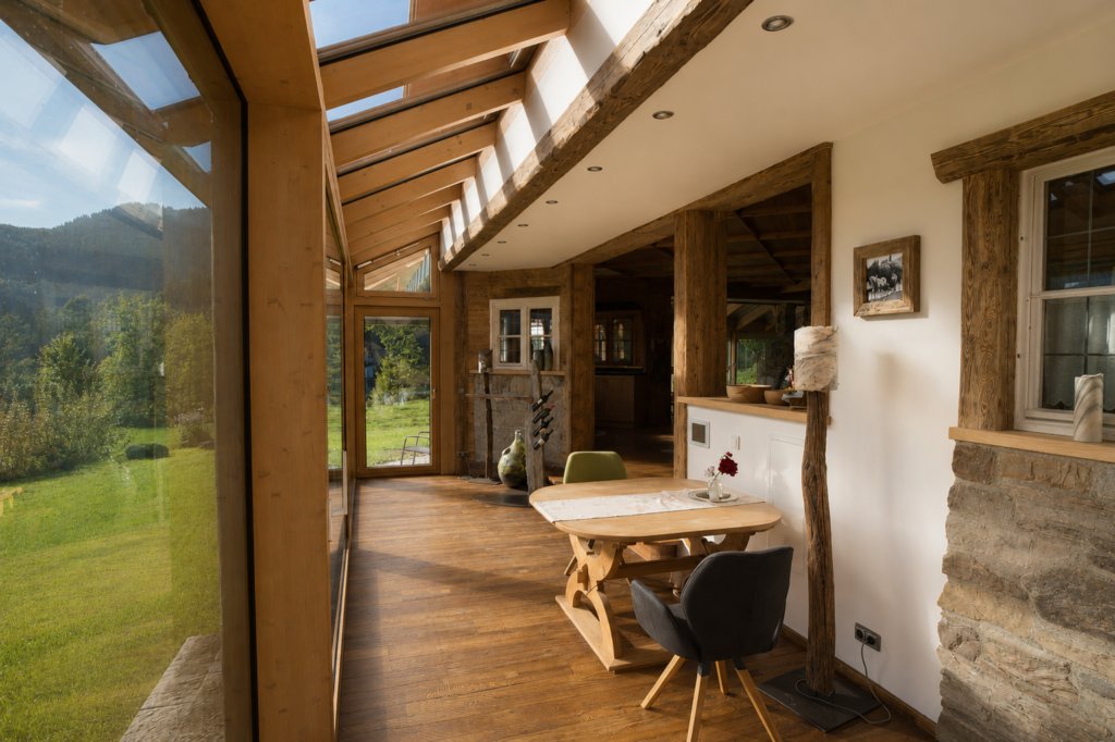 Heller, rustikaler Wintergarten mit Panoramafenstern, Holzkonstruktion und kleinem Essbereich.